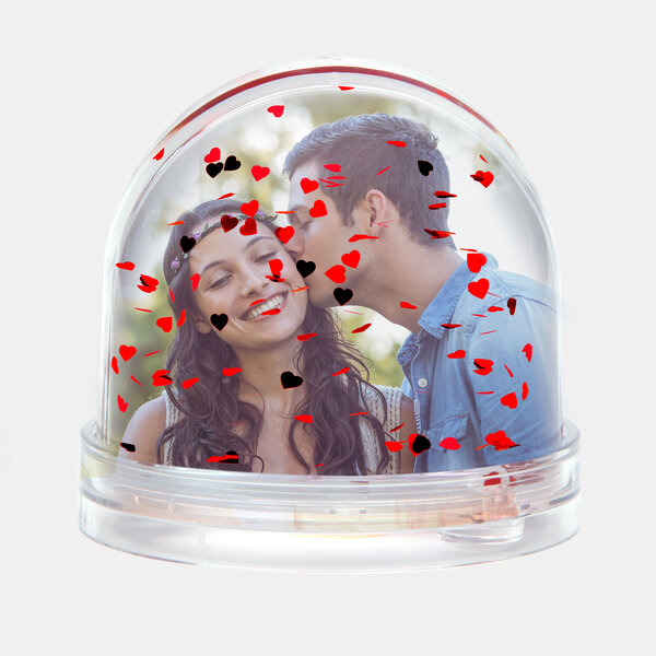 Die Schneekugel mit roten Herzen zeigt ein Paar, bei dem der Mann der Frau zärtlich auf die Wange küsst.