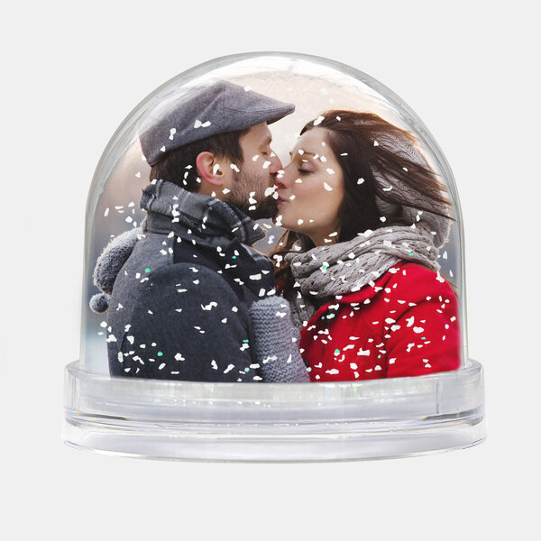 Die Schneekugel mit Schnee zeigt ein Paar im Wintermantel, das sich liebevoll vor einem Kuss anschaut.